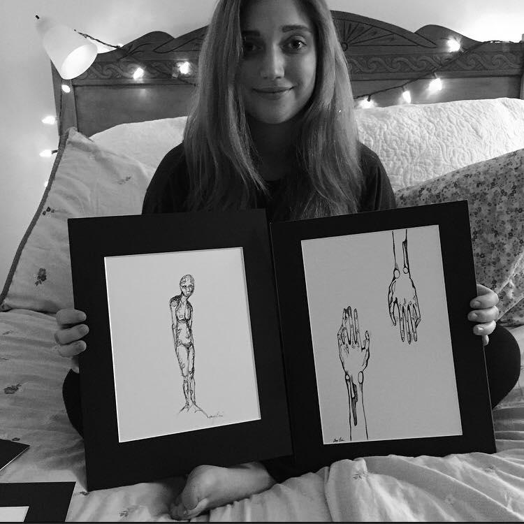 Ally Ellis holding her two of her sketches.