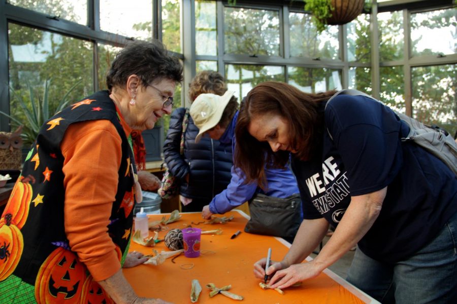 Volunteer Cathy Kennedy helps Pumpkin Festival attendees make corn husk dolls. Kennedy has been volunteering at the Pumpkin Festival for the past five years. “I just love the gardens, and I think [the Pumpkin Festival] is a wonderful community event. We get thousands of people who come and enjoy the gardens,” Kennedy said. 
