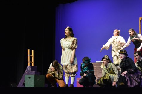Senior Nora Goudie, who plays Alice, stands on stage amidst other cast members. 