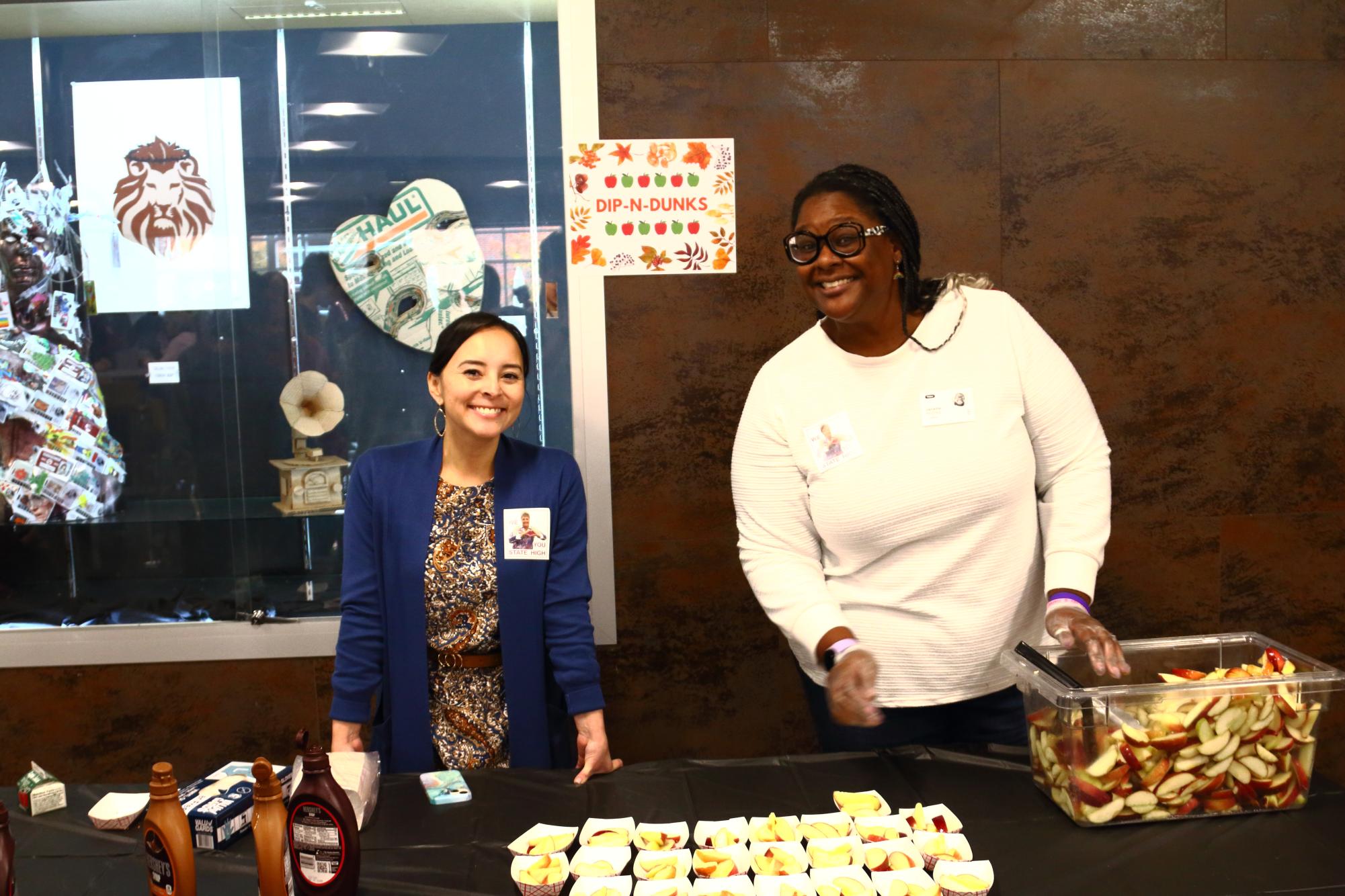 Staff members smile and hand out Fall Fest items in the cafeteria on Oct 30.
