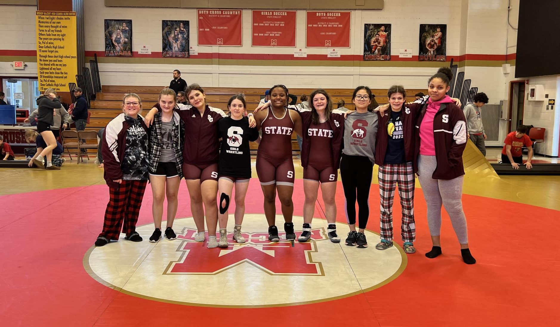 The State High girls wrestling team stands together at a tournament. 
