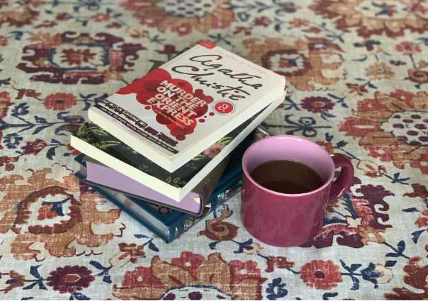 A stack of four classic books on a decorative table cloth next to a pink mug of coffee.