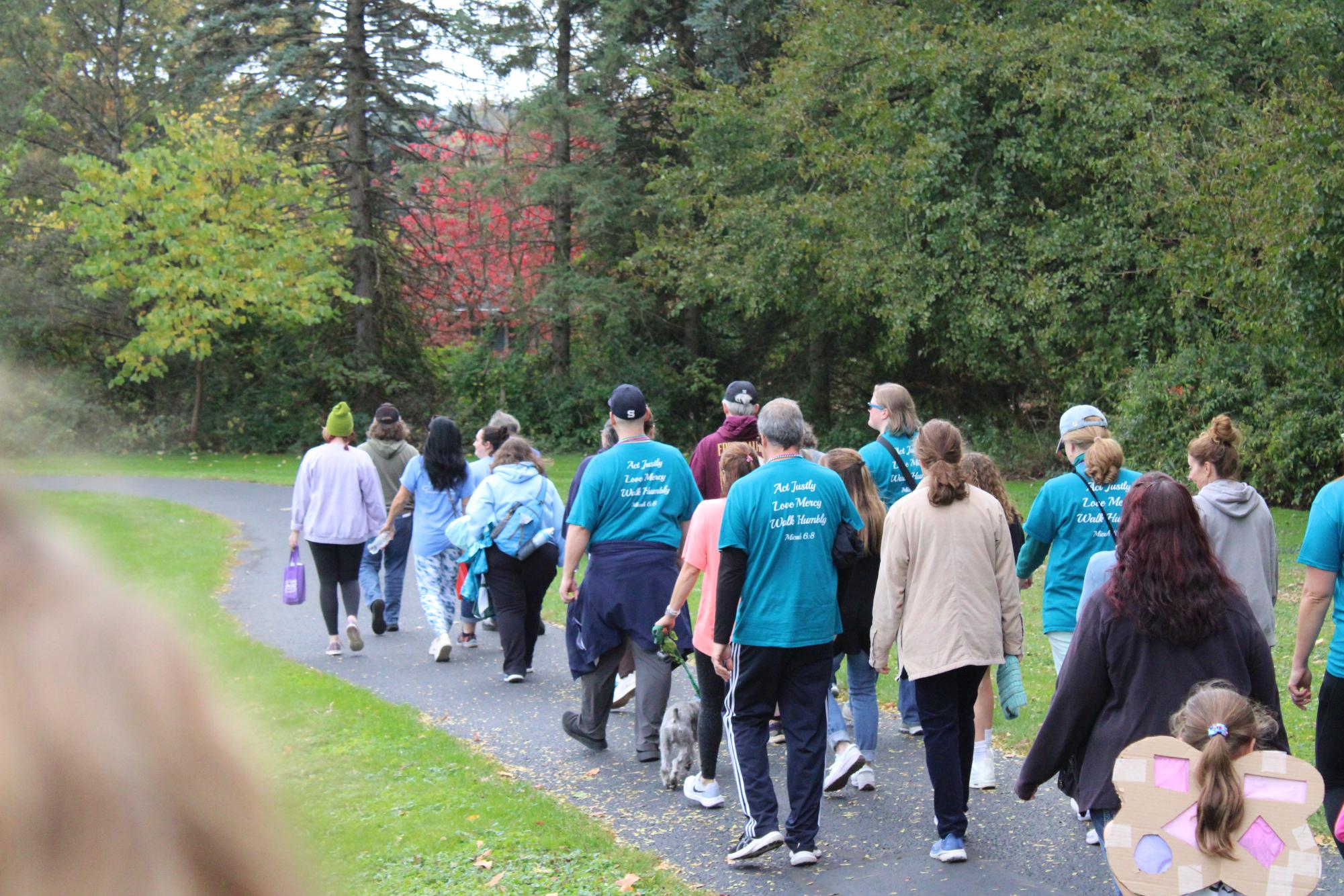 Participants (many of which are wearing blue shirts) walking down a path at Tudek Park during the Out of the Darkness Walk on October 13, 2024, with green trees in the background.