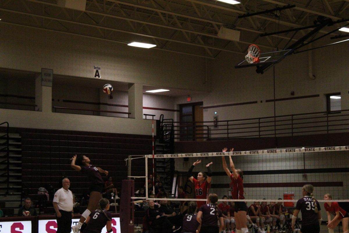 Senior Sarah Tate (25) hits a ball during the first set against Cumberland Valley. She is in the air, about to hit the ball, wearing a maroon shirt with #25 on it. On the opposite side of the net, the opponents are about to block.