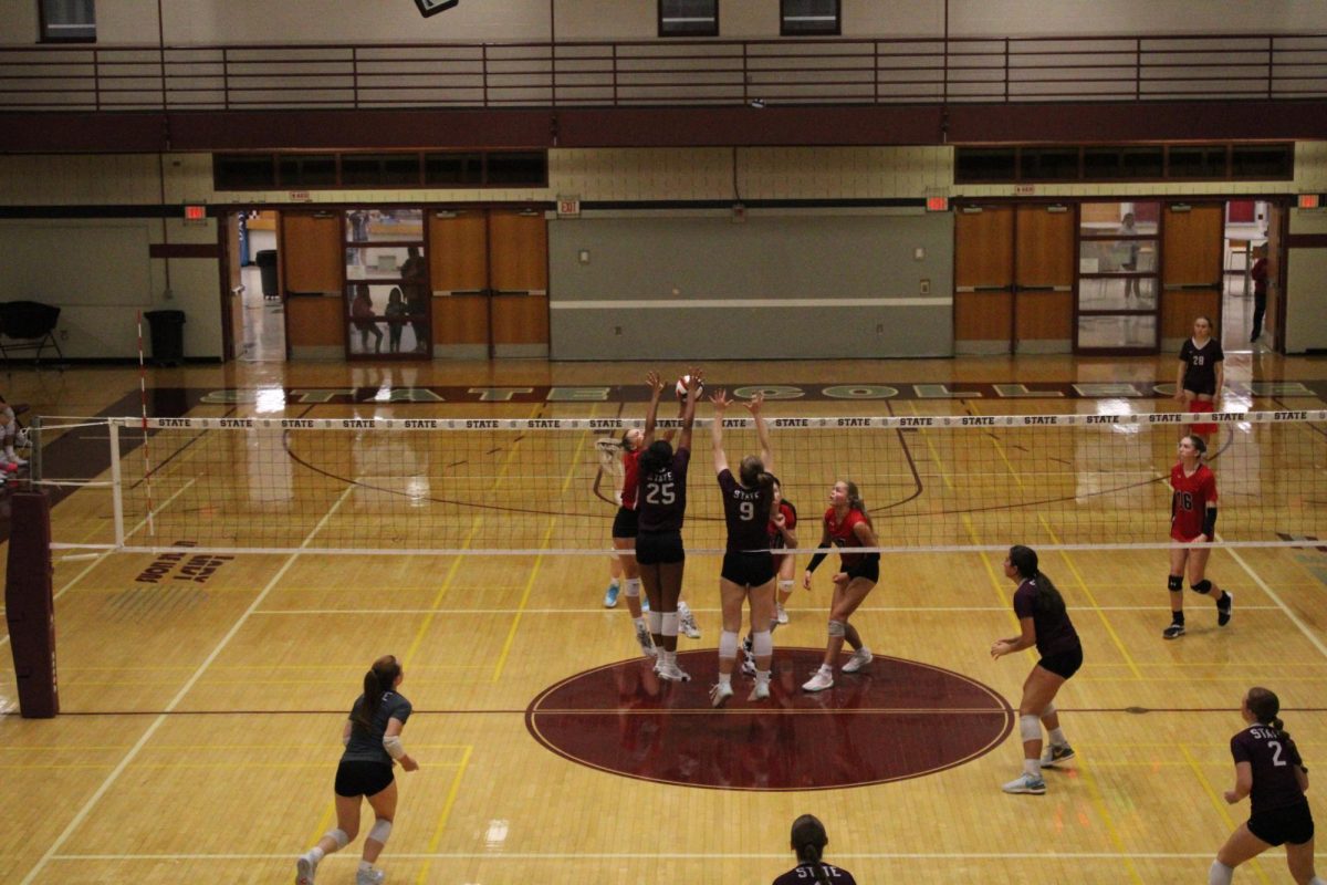 Seniors Alex Haskins (9) and Sarah Tate (25) score a point for State High early in the second set. They are blocking the ball, Sarah Tate to the left, Alex Haskins to the right, both jumping with their arms up