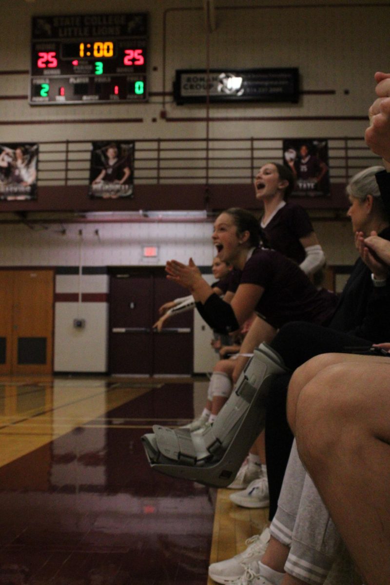 Junior Helena Woskob celebrates the last points of the third set. She is sitting on the bench and applauding. Other team mates are in the background