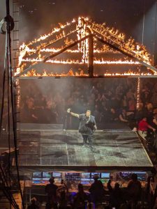 Jelly Roll tipping his hat to the crowd while standing under a burning structure during his performance at the Bryce Jordan Center.