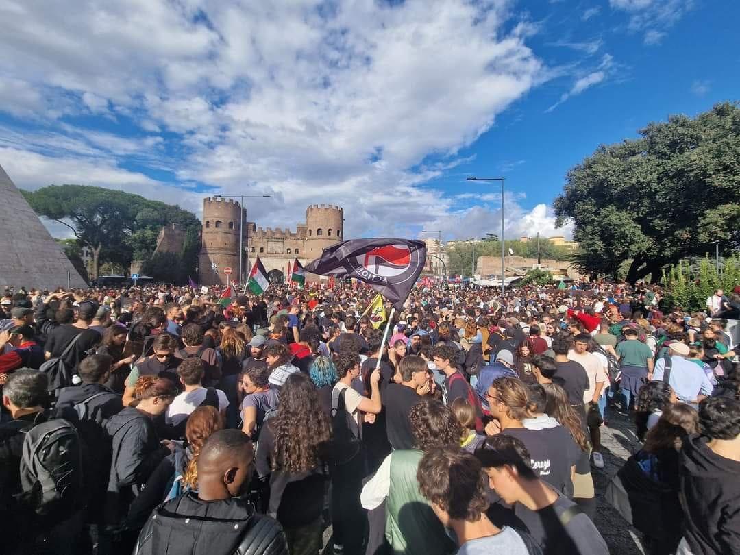 A full square in Rome, on Oct 5, at a pro Palestine protest. There are flags waving and Roman ruins in the background