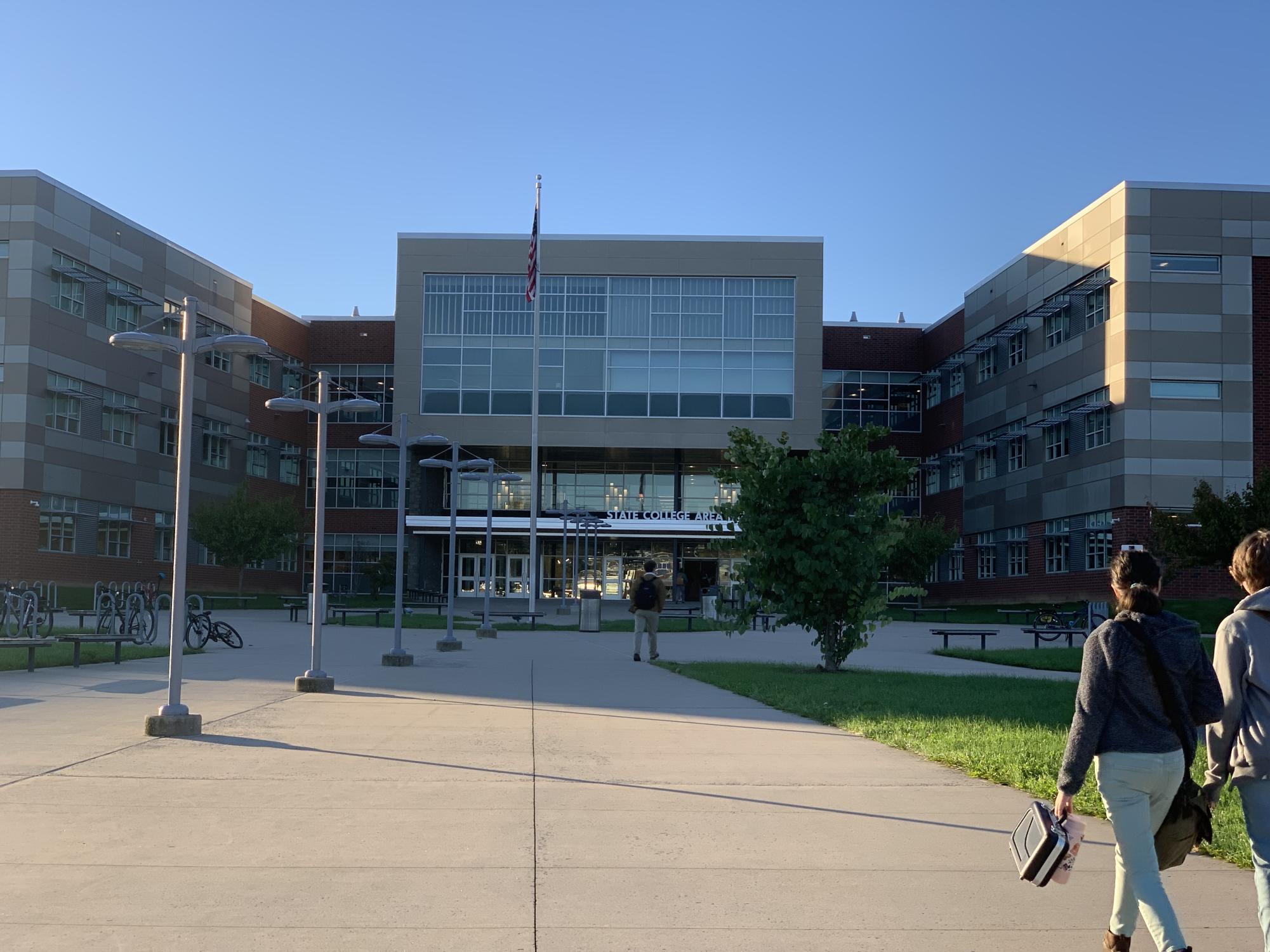 Students walking into the lower main entrance of State College Area High school on a clear sunny day.