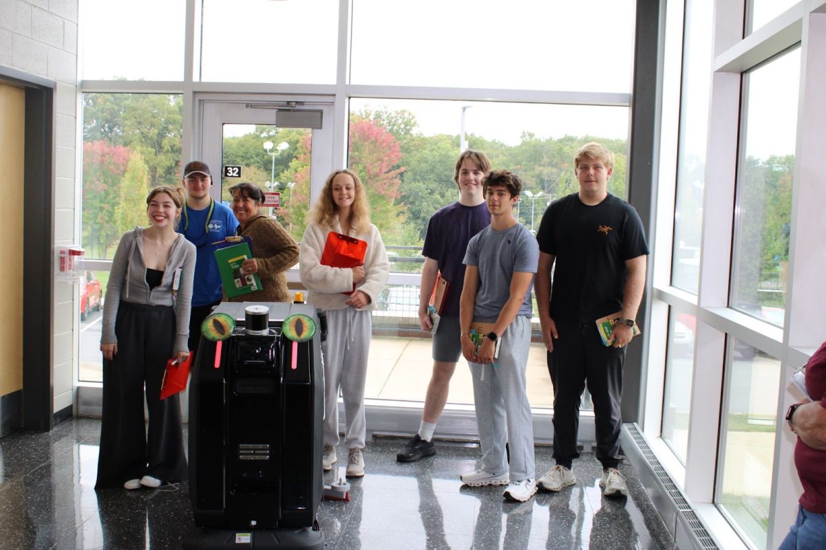 A group of students pose with the robot in the hallway. 