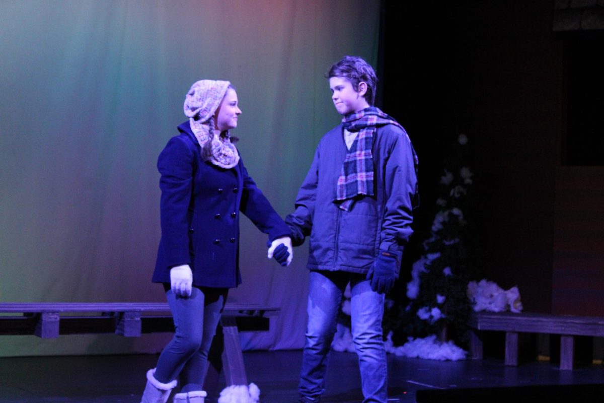 Ginette (Julia Oberholzer) and Pete (Finn McCutchen) hold hands in front of a bench.