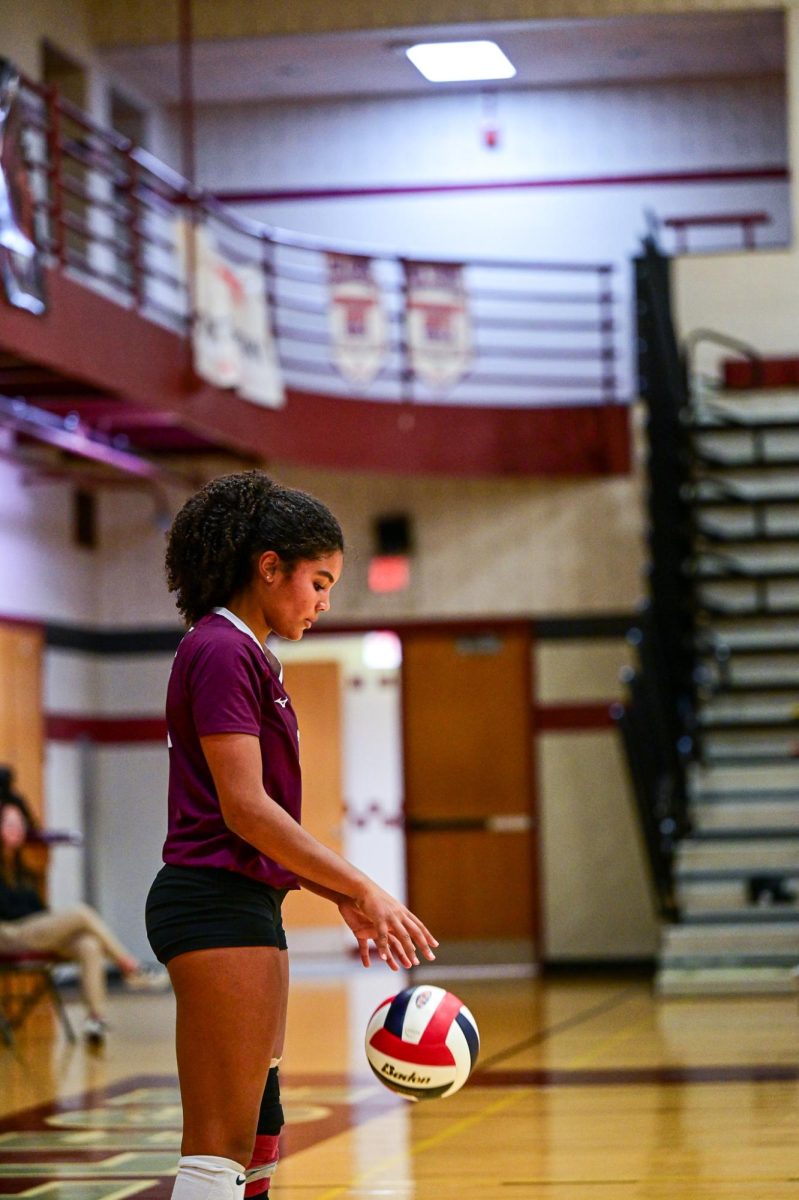 A SCAHS Girl's Volleyball player standing at the serve line looks down at a ball.