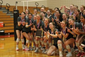 The entire State High Girls Volleyball team posing for a picture making a W with their hands while holding their Division Six Championship trophy.