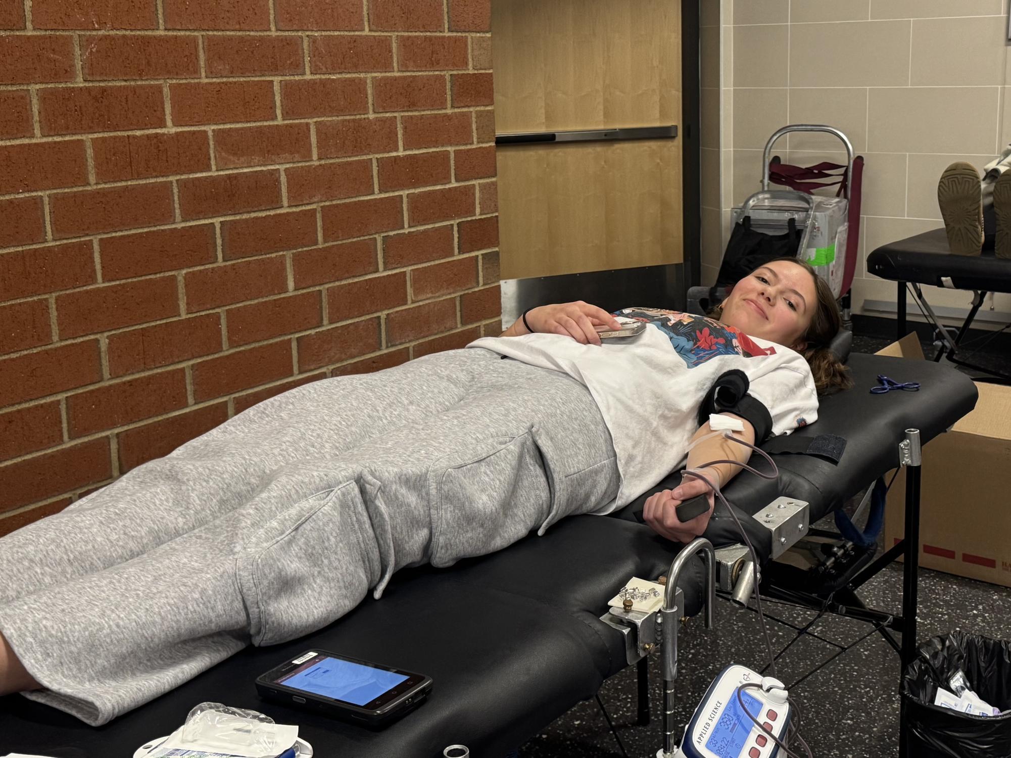 Emerson Wilson laying down on a bed while donating blood and looking at the camera.