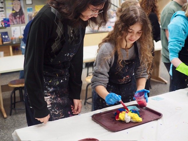 Ren Estep (left)and junior Lynette Hoffman (right) smile, chat, and add red colored dye to a tie-dye shirt at the November 19 Art Club event.