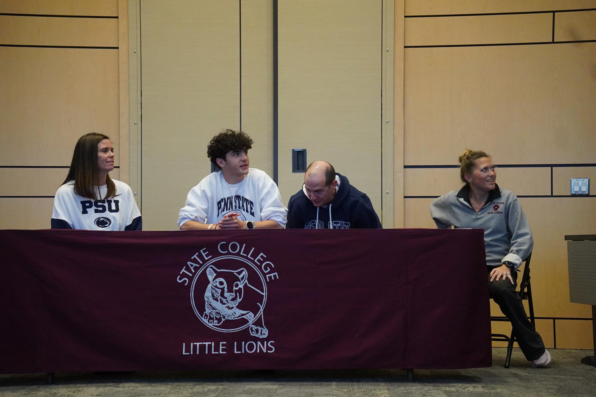 D1 Penn State cross country and track commit Isaac Oppermann sits at signing day, flanked by his parents and coach.