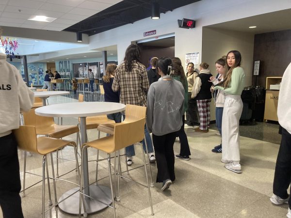 Students await to enter the food court during lunch, tables are seen on the left.