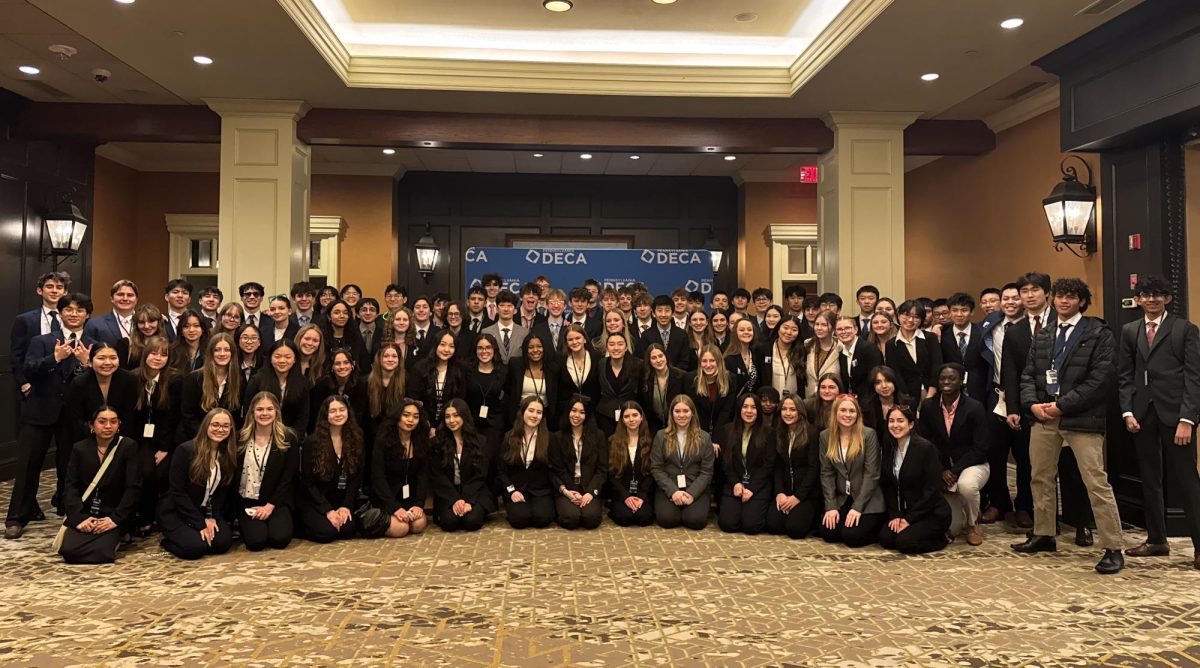 DECA members that qualified for states posing for a group picture in front of a DECA backdrop wearing business suits after competing in the states competition