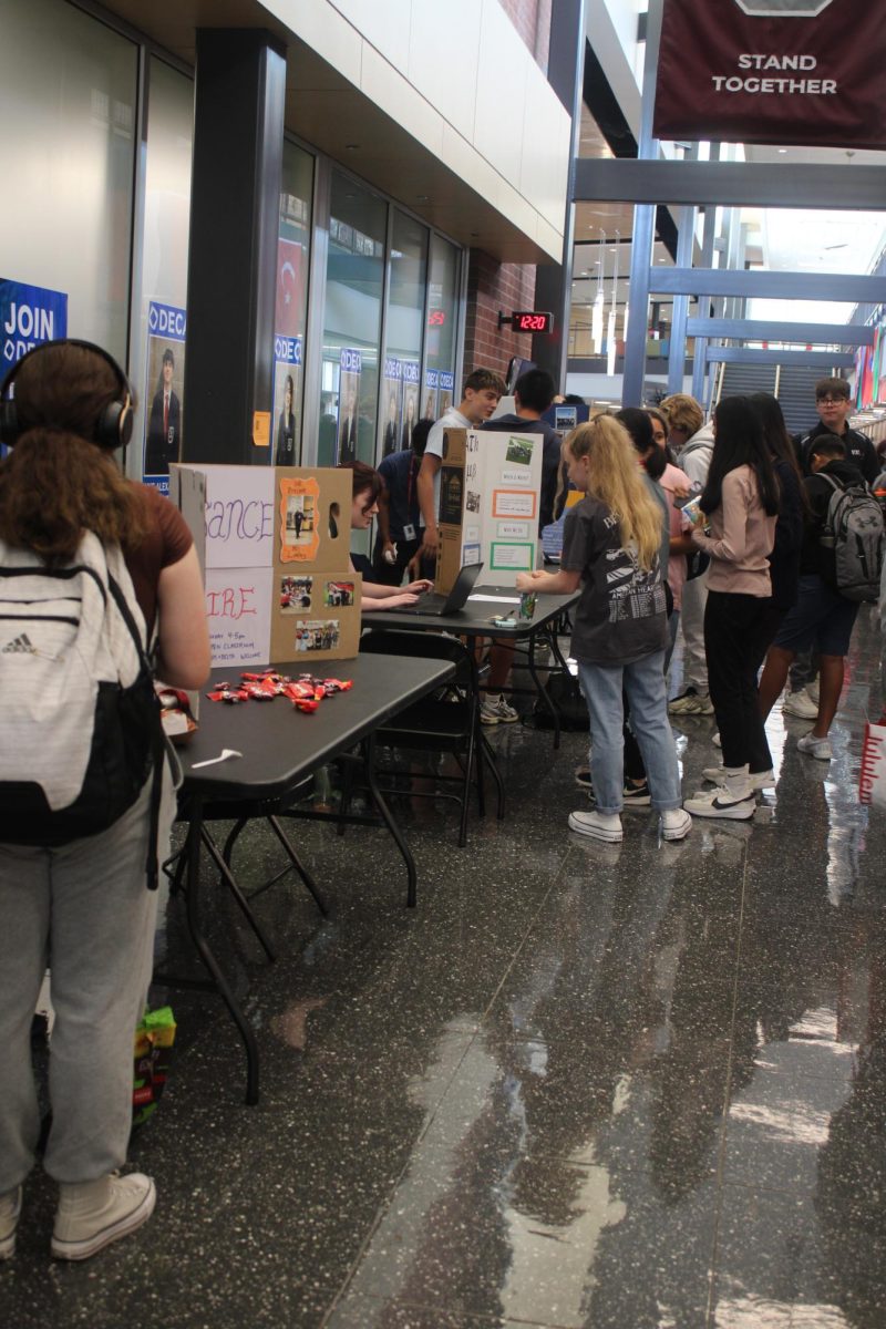Students looking at different poster set ups on tables and asking the club members, who are with the posters, what the club is about.