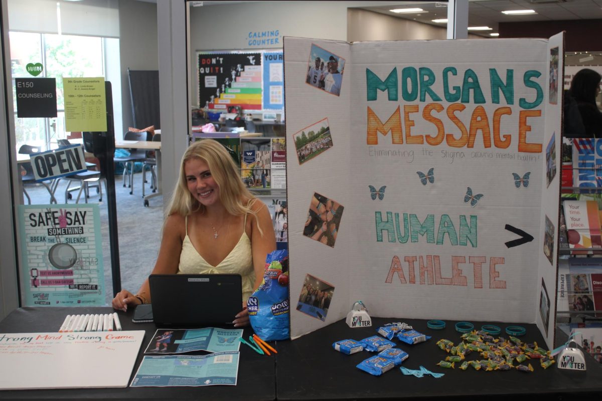 Member of Morgan’s Message, Alexandra Shilova, sits next to a poster board that describes how Morgan's Message advocates for athletes mental health.