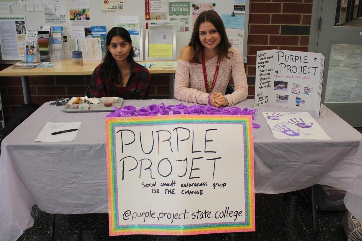 Two members of The Purple Project sit behind their poster board of their club and explain to students how this club advocates for sexual assault victims.