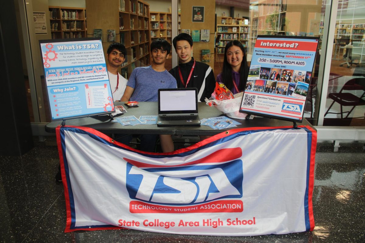 Four students sit behind a table set up for the Technology Students Association and try to recruit members.