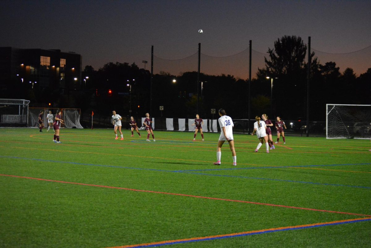 The soccer ball flies through the air as Katy Schmeck (goalie) kicks it back into the field. 