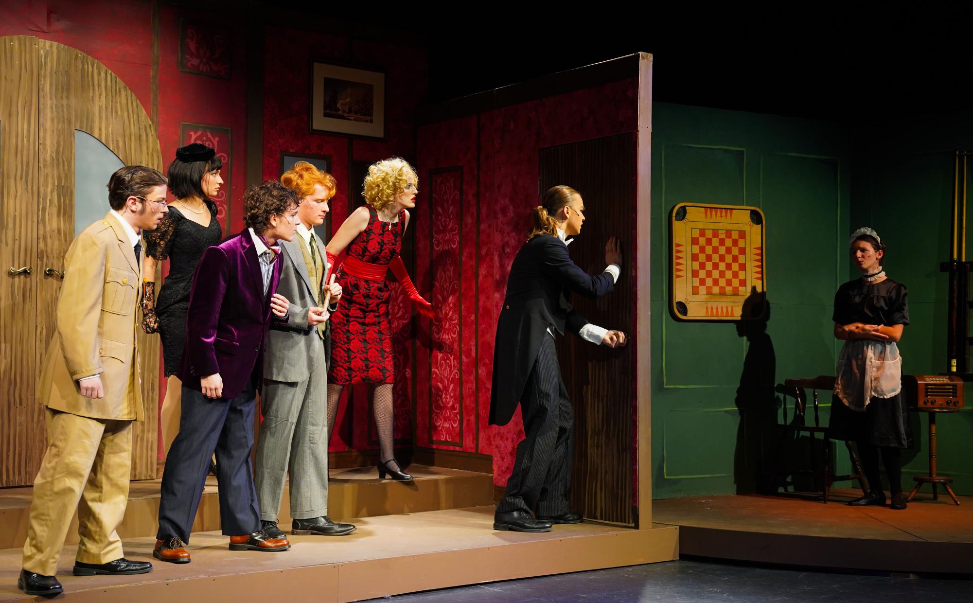 Colonel Mustard (Ben Ricker), Mrs. White (Anna Christopher), Professor Plum (Lincoln Sandoval-Strausz), Mr. Green (Henry Mathews), Miss Scarlett (Hannah Smith), and Wadsworth (Oscar Vebber) try to get to the screaming and frightened Yvette (Ali Schirf). 
