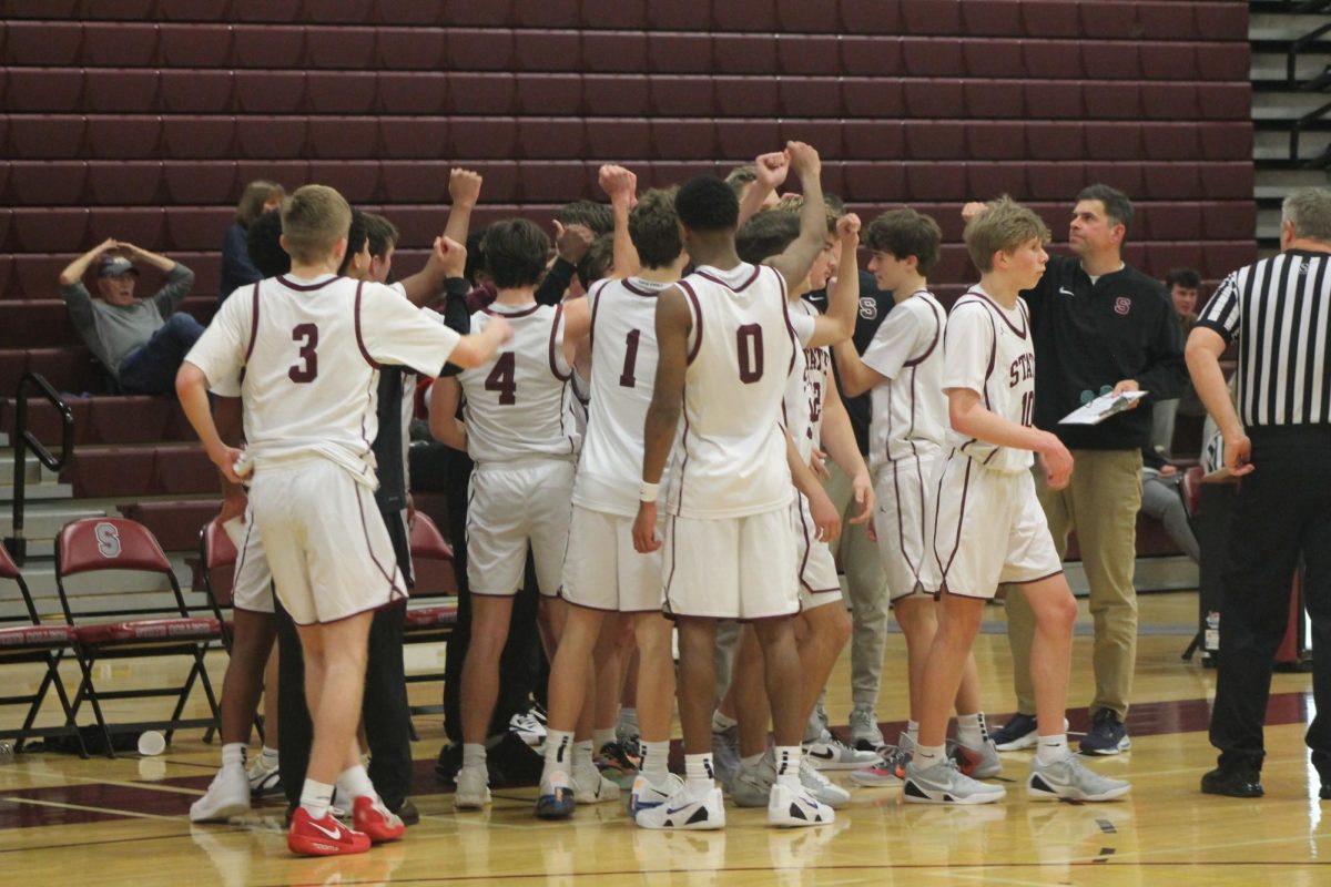 Multiple State players wearing white jerseys gathered in a group, with each player holding one of their arms in the air.