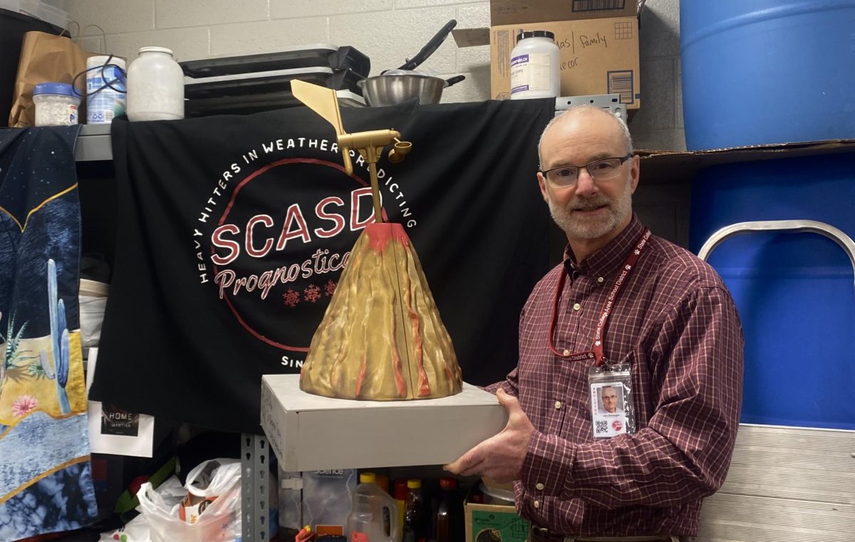 Mr. Donoughe holds the prognosticators' trophy in front of their team flag.