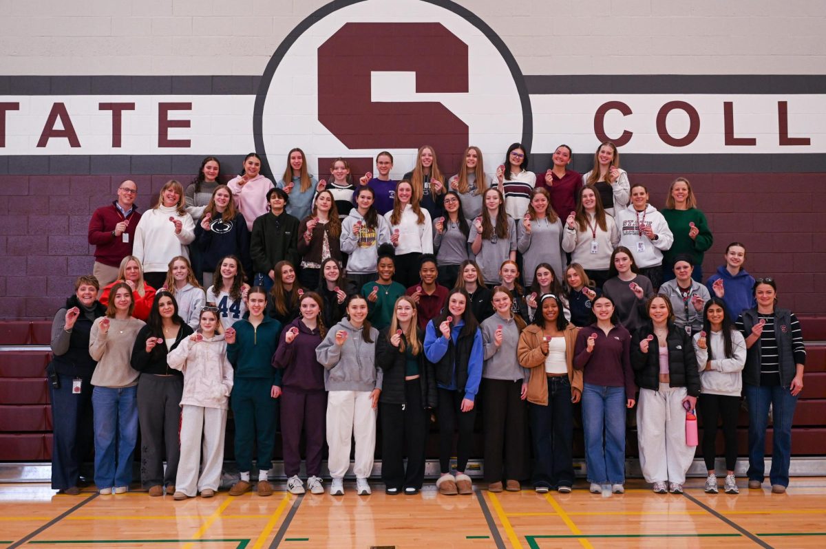 Faculty and students gather to take a group photo holding pride coins at the woman in sport event