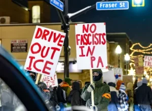 Protesters march around the corner of W Beaver Avenue and Fraser Street on the evening of Jan. 26, holding up signs that say “Drive out ICE” and “No Fascists in PA”. The protestors block traffic as three stand in the crosswalk. 