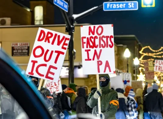 Protesters march around the corner of W Beaver Avenue and Fraser Street on the evening of Jan. 26, holding up signs that say “Drive out ICE” and “No Fascists in PA”. The protestors block traffic as three stand in the crosswalk. 